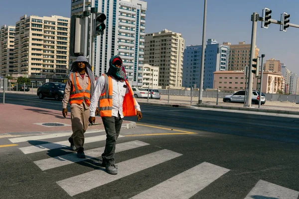 Başı bandajlı turuncu üniformalı işçiler, sıcak ve güneşli bir günde Güneş 'ten saklanıyor: Birleşik ARAB EMIRATES, DUBAI - 17 Ekim 2017.