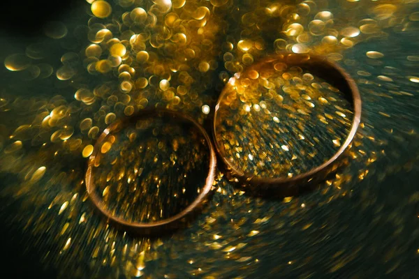Gold rings in gold sequins on a green background. Design for wedding rings with gold dust. Photography of jewelry. | YEKATERINBURG, RUSSIA - 05 JULY 2019.