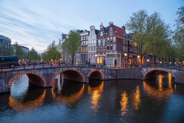 Beautiful night in Amsterdam. Night illumination of buildings and boats near the water in the canal.