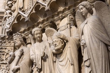 Dört büyük heykel, başı kesilmiş bir kral ve Aziz Denis 'i temsil ediyor. Kafasını taşıyor ve iki melek tarafından çevrelenmiş. Katolik katedralinin batı cephesi Notre-Dame de Paris.