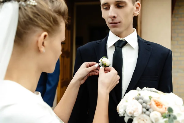 Невеста надевает бутоньерку на жениха — стоковое фото