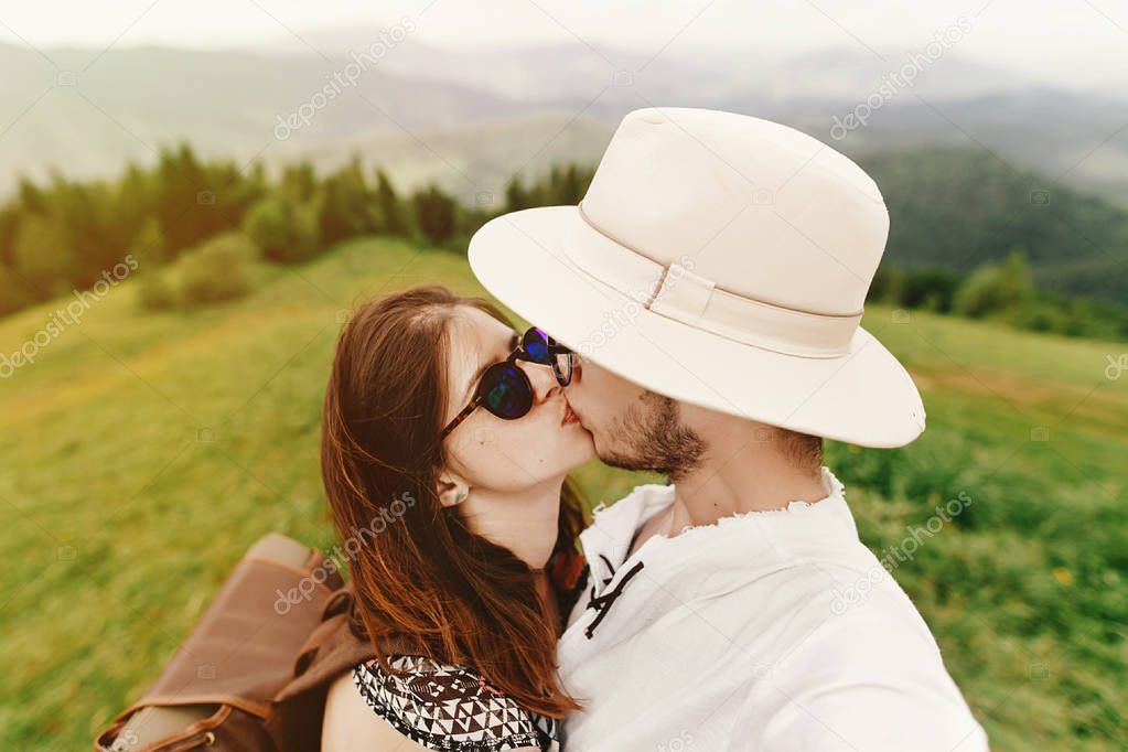 stylish  hipster couple traveling and kissing on top of mountain
