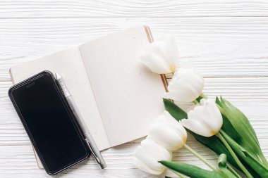 telefon ekranında, defter, kalem ve laleler