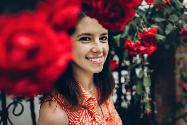 Chica sonriendo bajo grandes rosas rojas — Foto de Stock