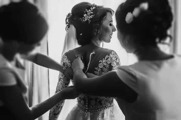 Bridesmaids helping bride fit in dress — Stock Photo, Image