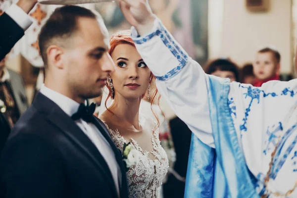 Bruid en bruidegom onder kronen in de kerk — Stockfoto