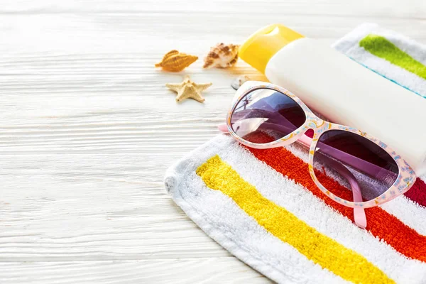 Handdoek, zonnebril, zonnebrandcrème en schelpen — Stockfoto