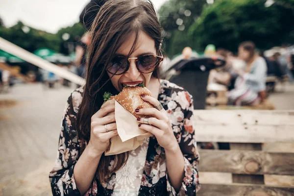Девушка в солнечных очках, кусающая гамбургер — стоковое фото