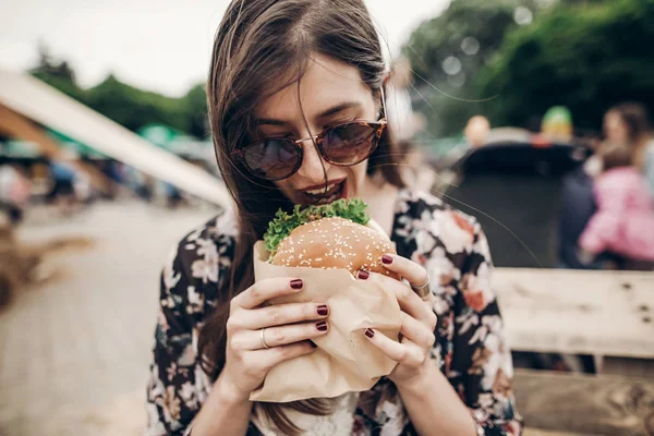 Menina em óculos de sol mordendo hambúrguer Fotos De Bancos De Imagens