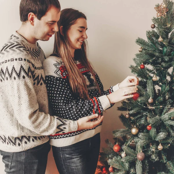 居心地の良い部屋にクリスマス ツリーを飾るスタイリッシュなセーターの幸せカップル — ストック写真