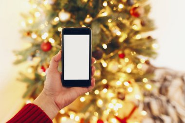 telefon ile boş perde güzel Noel ağacı ışıkları arka plan üzerinde tutan el