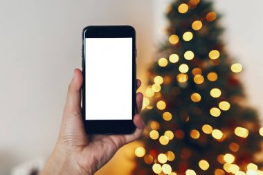telefon ile boş perde güzel Noel ağacı ışıkları arka plan üzerinde tutan el