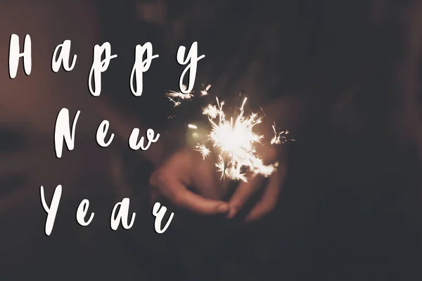 Feliz año nuevo letrero de texto, la mano con una bengala chispa ardiente fuegos artificiales — Foto de Stock