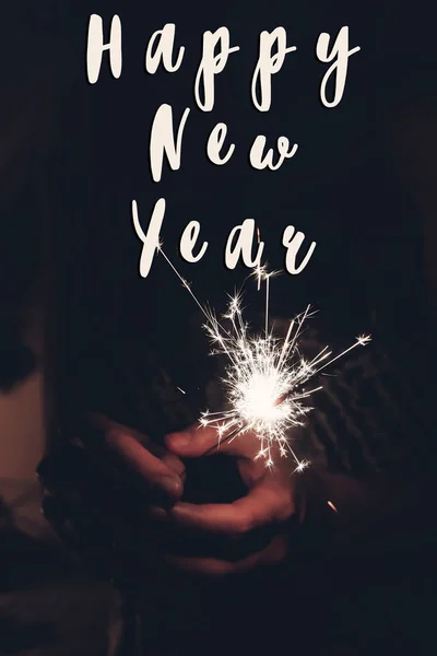 Happy new year text sign, hand holding a burning sparkler firework bengal light . — стоковое фото