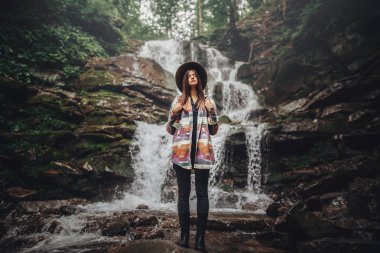 şelale, rahatlatıcı şapkalı şık Gezgin kız atmosferik an. hipster kadınla ormandaki nehir saatte sırt çantası. metin için yer. Yolculuk tutkusu ve seyahat kavramı