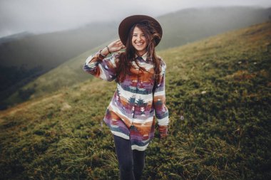 mutlu traveler kız sırt çantası ayakta dağlarda şapkalı. rüzgarlı dağın tepesinde gülümseyen hipster kadın. metin için yer. Yolculuk tutkusu ve seyahat kavramı. Atmosferik epik an