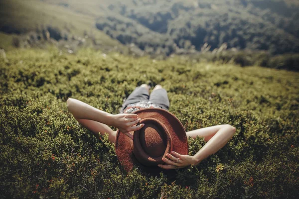 时髦的旅行者女人躺在草地上 在山上放松 在山顶上的时髦女孩 帽子在她的脸上 文本空间 大气时刻 癖与旅游理念 — 图库照片