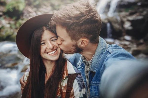 森の中の滝で幸せな流行に敏感なカップルを Selfie スタイリッシュな家族旅行を抱きしめるとキス — ストック写真