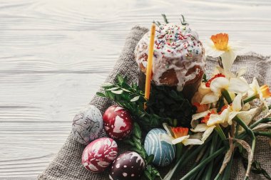 Şık paskalya ekmeği ve sade ahşap arka planda mum sarısı çiçekler ve yeşillikle boyanmış yumurtalar. Mutlu Paskalyalar, tebrik kartı. Metin için boşluk