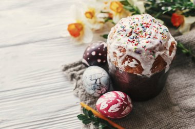 Şık paskalya ekmeği ve sade ahşap arka planda mum sarısı çiçekler ve yeşillikle boyanmış yumurtalar. Mutlu Paskalyalar, tebrik kartı. Metin için boşluk