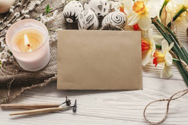 Modern Paskalya yortusu yumurta ve taze bahar çiçekleri rustik zemin üzerine nergis. Mutlu Paskalya tebrik kartı ile metin için yer. şık boyalı yumurta. Kraft kağıt