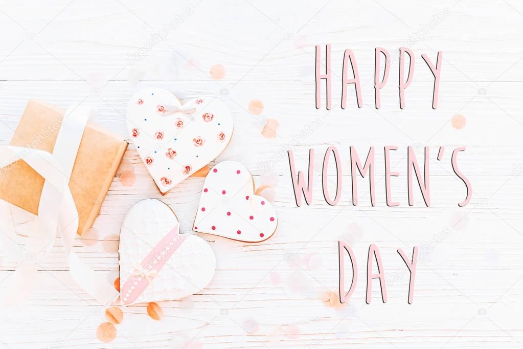 happy women's day text sign flat lay. 8 march. pink hearts and present and confetti on white rustic wooden background. space for text. greeting card concept. womens bright image