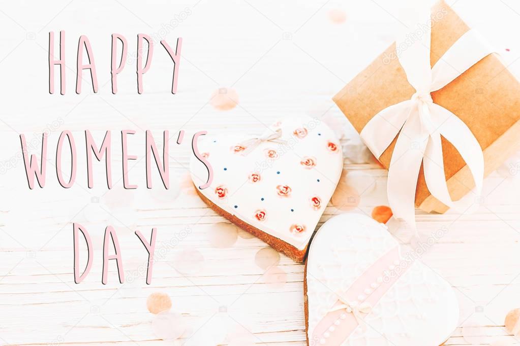 happy women's day text sign flat lay. 8 march. pink hearts flowers and present box on white rustic wooden background. space for text. greeting card concept. womens bright image