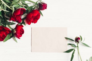 güzel kırmızı peonies buket ve craft kağıt Beyaz ahşap rustik zemin, düz kartına yatıyordu. metin için yer ile modern tebrik kartı. Üstten Görünüm.