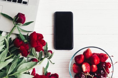 dizüstü bilgisayar, smartphone, çilek, kiraz ve güzel kırmızı peonies düz beyaz ahşap zemin üzerinde yatıyordu