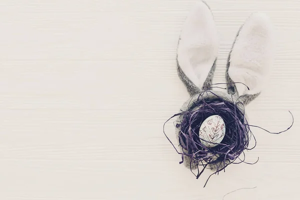 复活节快乐的概念 兔子耳朵和时髦的蛋在巢在白色木背景平放置与空间为文本 创造性的复活节形象 季节贺卡模拟 — 图库照片