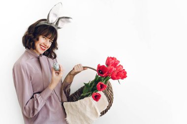 Paskalya AVI kavramı. sepet laleler ve Paskalya yumurtası ayakta beyaz arka planda tutan güzel şık kız