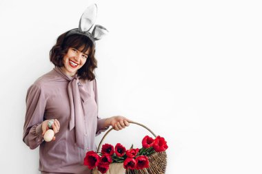 Paskalya AVI kavramı. sepet laleler ve Paskalya yumurtası ayakta beyaz arka planda tutan güzel şık kız