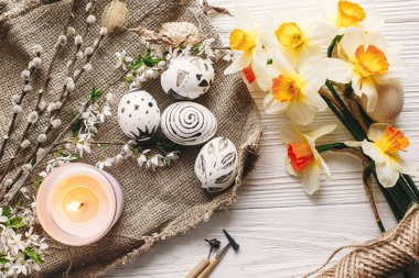 rustik ahşap arka plan bahar çiçekleri nergis ve mum ile şık boyalı Paskalya yortusu yumurta siyah ve beyaz renklere. Mutlu Paskalya tebrik kartı. Modern Paskalya yumurtaları görünümü top