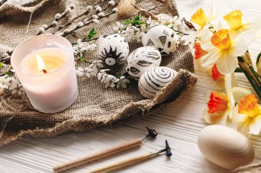 rustik ahşap arka plan bahar çiçekleri nergis ve mum ile şık boyalı Paskalya yortusu yumurta siyah ve beyaz renklere. Mutlu Paskalya tebrik kartı. Modern Paskalya yumurtaları görünümü top