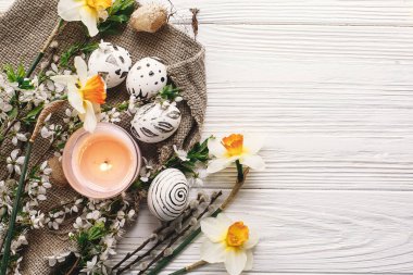 rustik ahşap arka plan bahar çiçekleri nergis ve mum ile şık boyalı Paskalya yortusu yumurta siyah ve beyaz renklere. Mutlu Paskalya tebrik kartı. görünümü, metin için yer modern Paskalya yumurta top