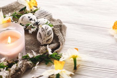 rustik ahşap arka plan bahar çiçekleri nergis ve mum ile şık boyalı Paskalya yortusu yumurta siyah ve beyaz renklere. Mutlu Paskalya tebrik kartı. görünümü, metin için yer modern Paskalya yumurta top