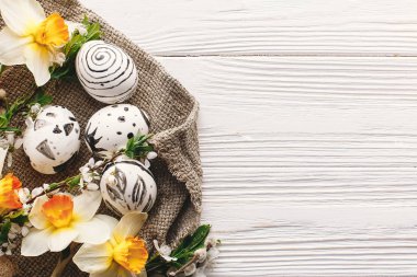 şık Paskalya düz yatıyordu. rustik ahşap arka plan bahar çiçekleri nergis ile boyanmış Paskalya yumurtası siyah ve beyaz renklere. Mutlu Paskalya tebrik kartı. Modern Paskalya üstten görünüm, metin için yer