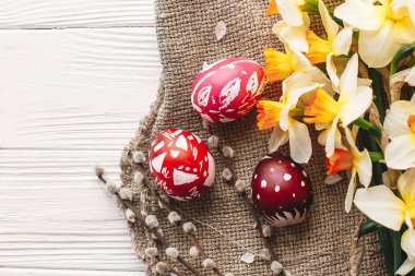 rustik ahşap arka plan bahar çiçekleri ve Söğüt dalları üzerinde şık boyalı Paskalya yumurta. Mutlu Paskalya tebrik kartı düz yatıyordu. metin için yer. Modern renkli Paskalya yumurtaları