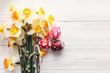 rustik ahşap arka plan bahar çiçekleri ve Söğüt dalları üzerinde şık boyalı Paskalya yumurta. Mutlu Paskalya tebrik kartı düz yatıyordu. metin için yer. Modern renkli Paskalya yumurtaları