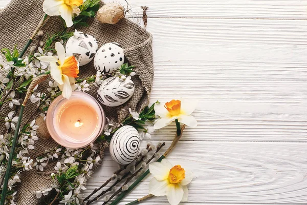 rustik ahşap arka plan bahar çiçekleri nergis ve mum ile şık boyalı Paskalya yortusu yumurta siyah ve beyaz renklere. Mutlu Paskalya tebrik kartı. görünümü, metin için yer modern Paskalya yumurta top