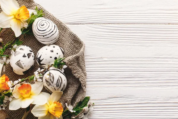 şık Paskalya düz yatıyordu. rustik ahşap arka plan bahar çiçekleri nergis ile boyanmış Paskalya yumurtası siyah ve beyaz renklere. Mutlu Paskalya tebrik kartı. Modern Paskalya üstten görünüm, metin için yer