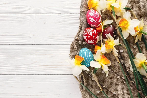 rustik ahşap arka plan bahar çiçekleri ve Söğüt dalları üzerinde şık boyalı Paskalya yumurta. Mutlu Paskalya tebrik kartı düz yatıyordu. metin için yer. Modern renkli Paskalya yumurtaları