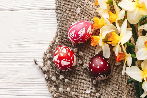 rustik ahşap arka plan bahar çiçekleri ve Söğüt dalları üzerinde şık boyalı Paskalya yumurta. Mutlu Paskalya tebrik kartı düz yatıyordu. metin için yer. Modern renkli Paskalya yumurtaları