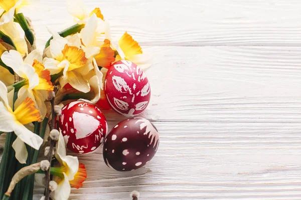 şık Paskalya düz yatıyordu. boyalı yumurta rustik ahşap arka plan bahar çiçekleri ve Söğüt dalları üzerinde. Mutlu Paskalya tebrik kartı. metin için yer. Modern renkli Paskalya yumurtaları