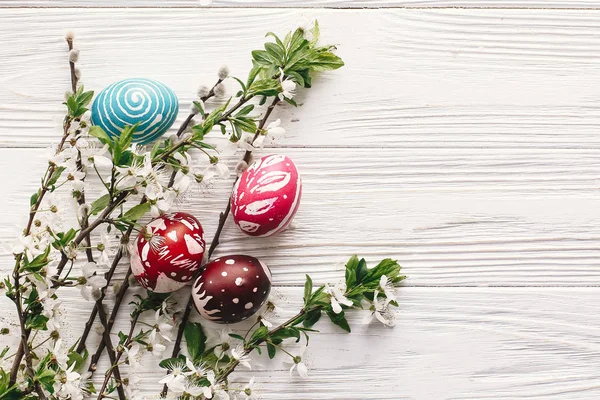rustik ahşap arka plan bahar çiçekleri ve Söğüt dalları üzerinde şık boyalı Paskalya yumurta. Mutlu Paskalya tebrik kartı düz yatıyordu. metin için yer. Modern renkli Paskalya yumurtaları