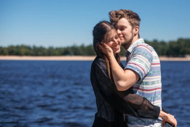 şık hipster çift yavaşça yaz şehirde rüzgarlı River sarılma. onun güzel kadınla öpüşürken ve güneşli kumsalda gülümseyerek mutlu bir adam. birlikte seyahat. şehvetli kucaklama an