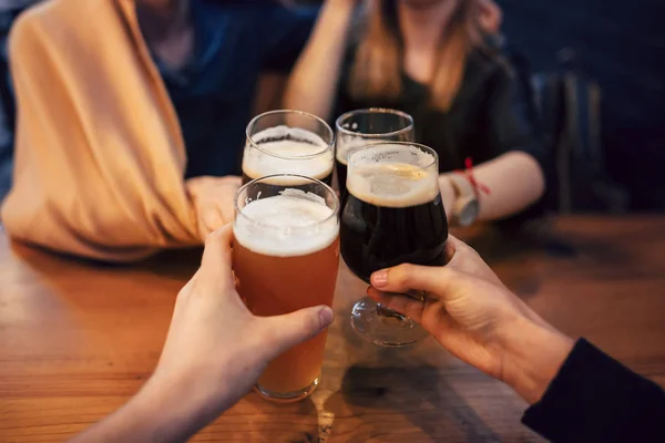 friends clinking and toasting with delicious craft beer in bar. group of people cheering and enjoying a beer in pub. hands holding glasses of beer. leisure and friendship  concept