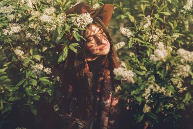 akşam güneş ışığı altında Gölgeler arasında çiçekli yeşil poz şapkalı güzel hippi kız bırakır. şık kadın Gezgin bahar bahçe sakin portre. metin için yer. Atmosferik an