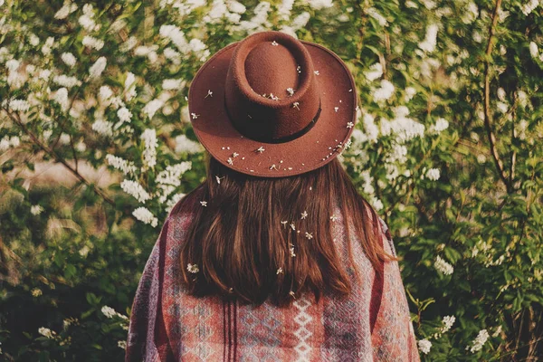 时尚时髦的女孩在帽子覆盖花摆在公园 后视图 — 图库照片