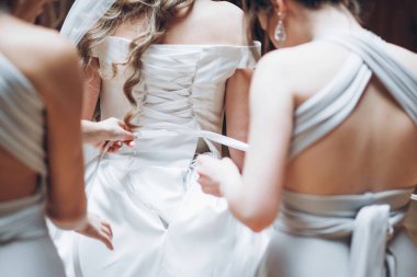 nedime gelin sabah otel odasında giyiniyor. Kızlar gelin şık elbisesi giyip geri şeritler ve el koymak yardım. hazırlanıyor